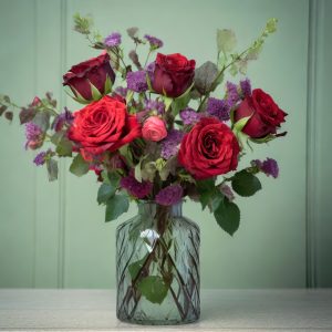 Rosas rojas en un jarrón de cristal minimalista con en un fondo de pared verde y mesa clara